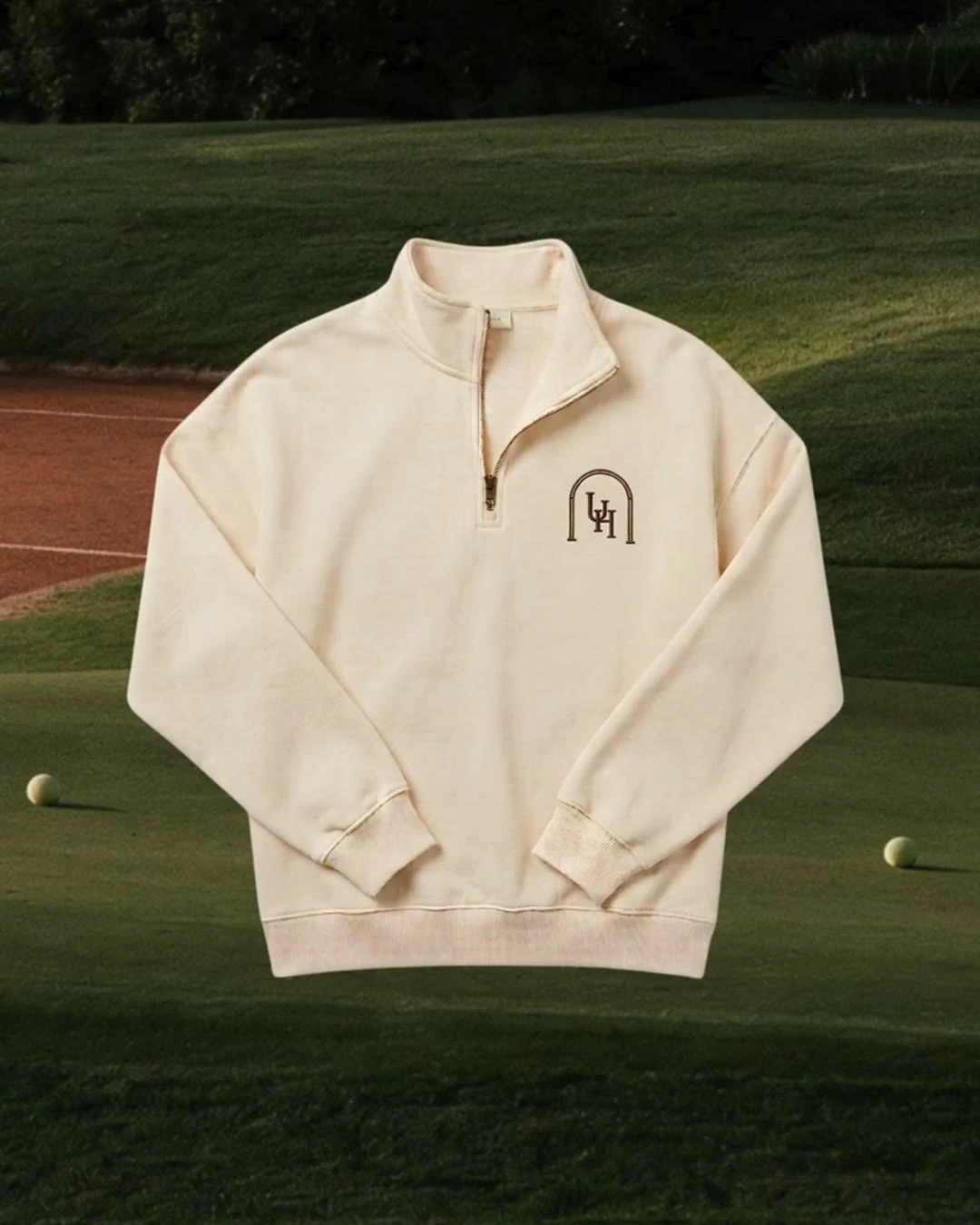 A cream Upper Heritage quarter-zip with the embroidered crest, shown against a fairway
