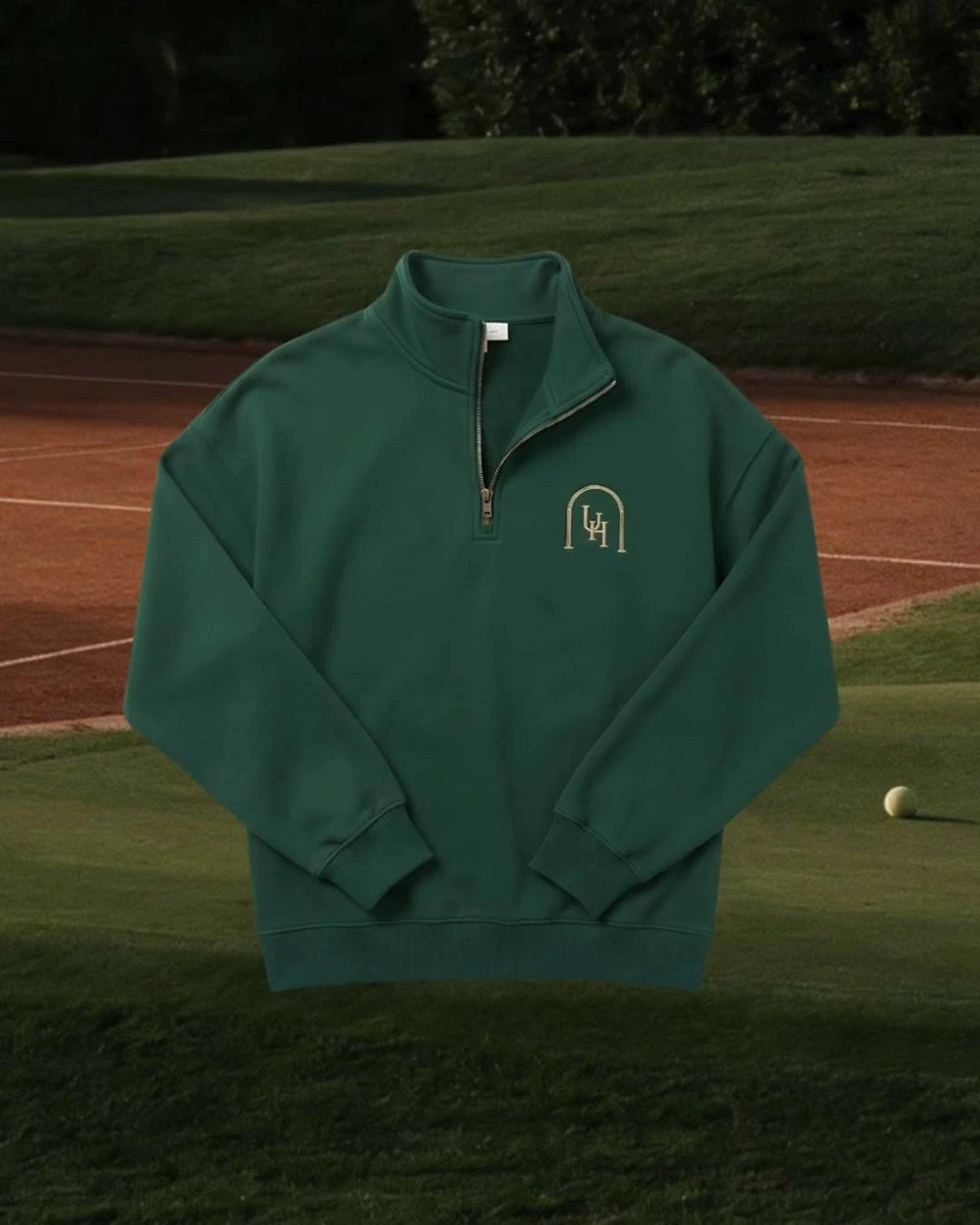 A deep-green Upper Heritage quarter-zip with the embroidered crest, shown against a fairway