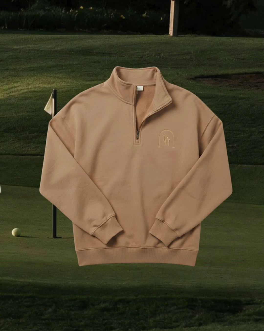 A sand-coloured Upper Heritage quarter-zip with the embroidered crest, shown against a fairway